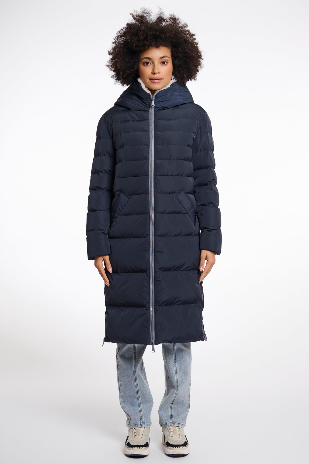 Person wearing a long navy blue puffer coat on a white background