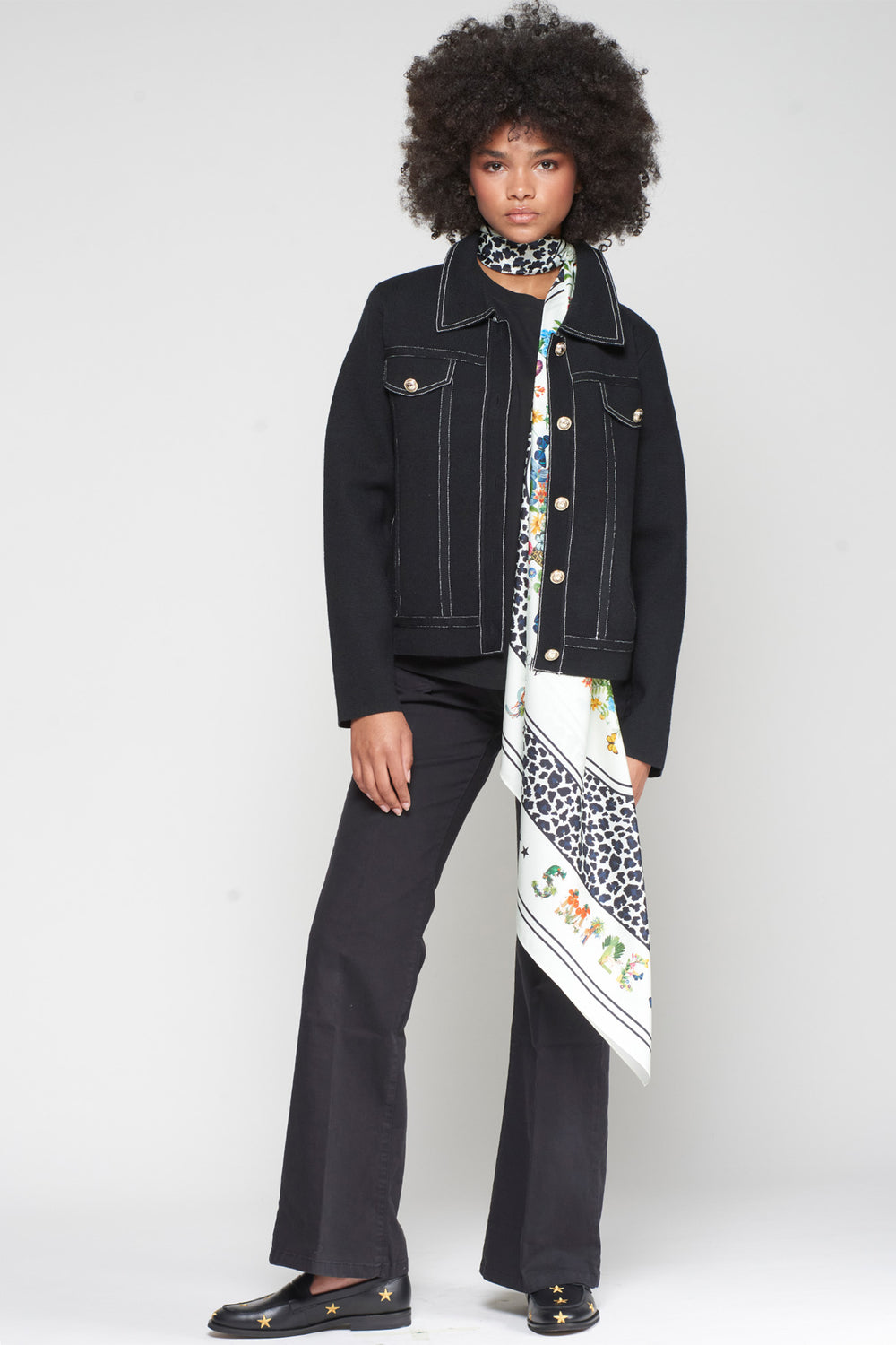 Person wearing a black jacket and pants with a colorful scarf, standing against a white background