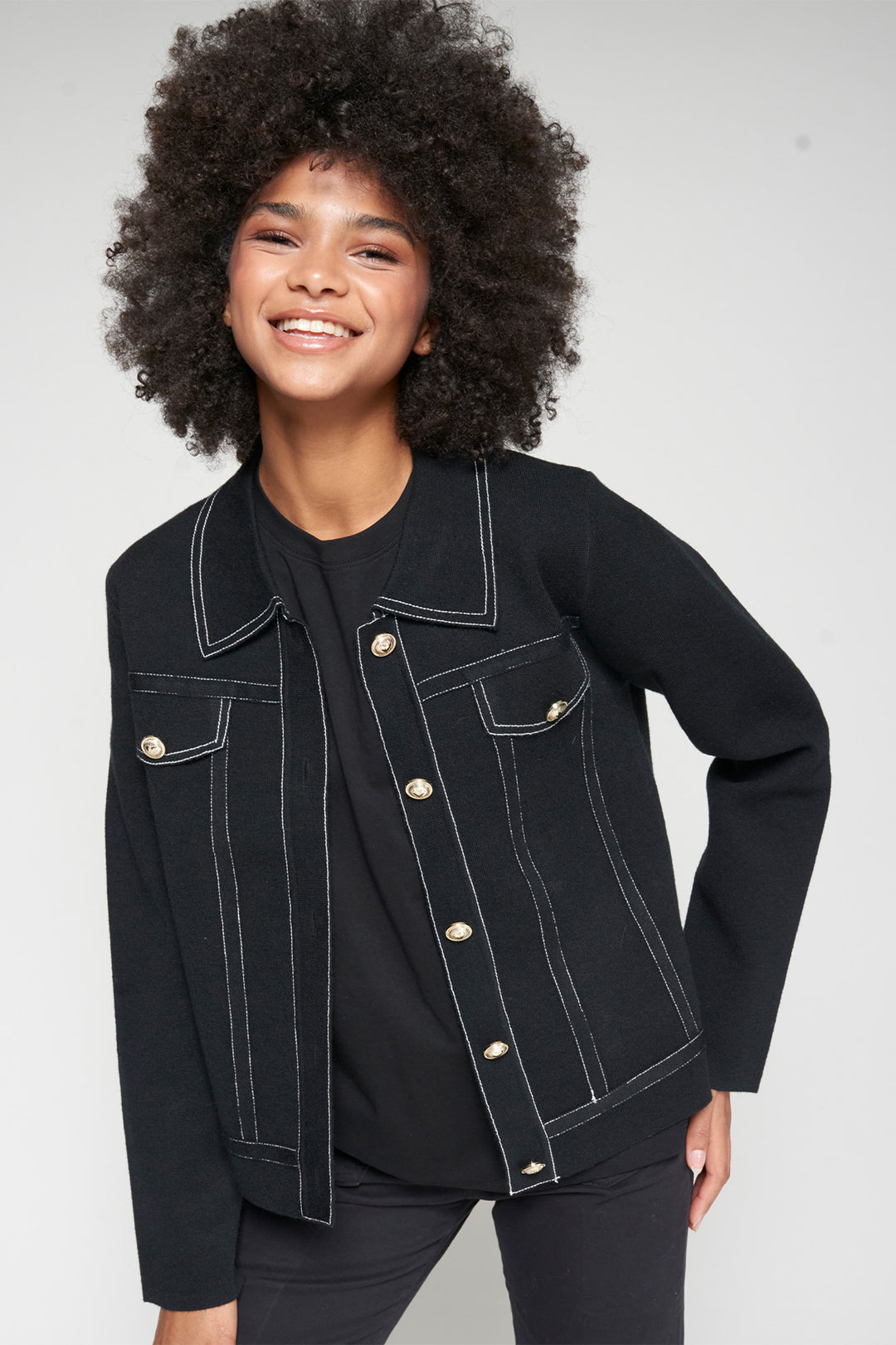 Woman wearing a black denim jacket with white stitching on a plain background